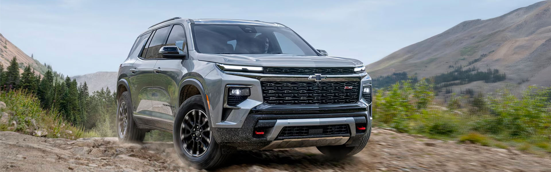 2026 Chevrolet Traverse midsize SUV driving off-road through a rugged mountain landscape.