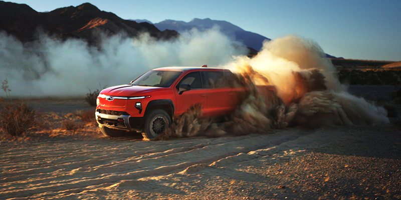 A Chevrolet Blazer driving through a vast desert landscape under a clear blue sky, showcasing the 2026 Silverado EV.