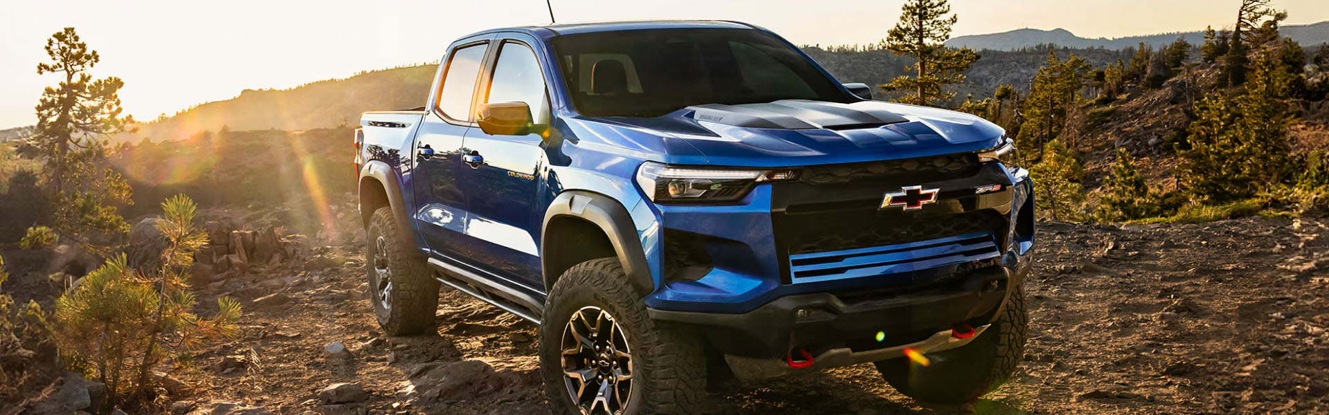 2026 Chevy Colorado ZR2 blue midsize pickup truck driving on a rugged off-road mountain trail